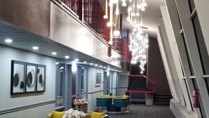 A hotel lobby with a patterned carpet, blue and yellow seating, a staircase, and a red railing.