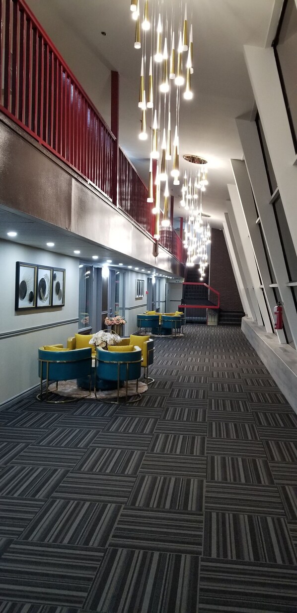 A hotel lobby with a patterned carpet, blue and yellow seating, a staircase, and a red railing.