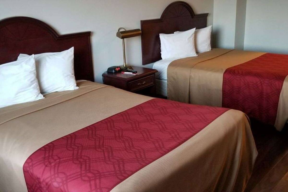 Two double beds with wooden headboards, a bedside table with a lamp, and a red patterned bedspread.