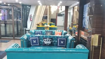A teal sofa with decorative pillows in a modern lobby area with wooden flooring and glass doors.