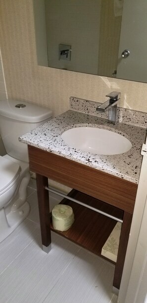 Un baño con un lavamanos blanco, un espejo encima y un inodoro a la izquierda.