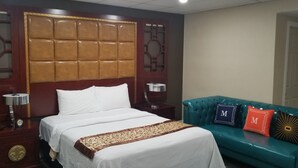 A hotel room with a large bed, a teal sofa with decorative pillows, and a traditional wooden headboard.