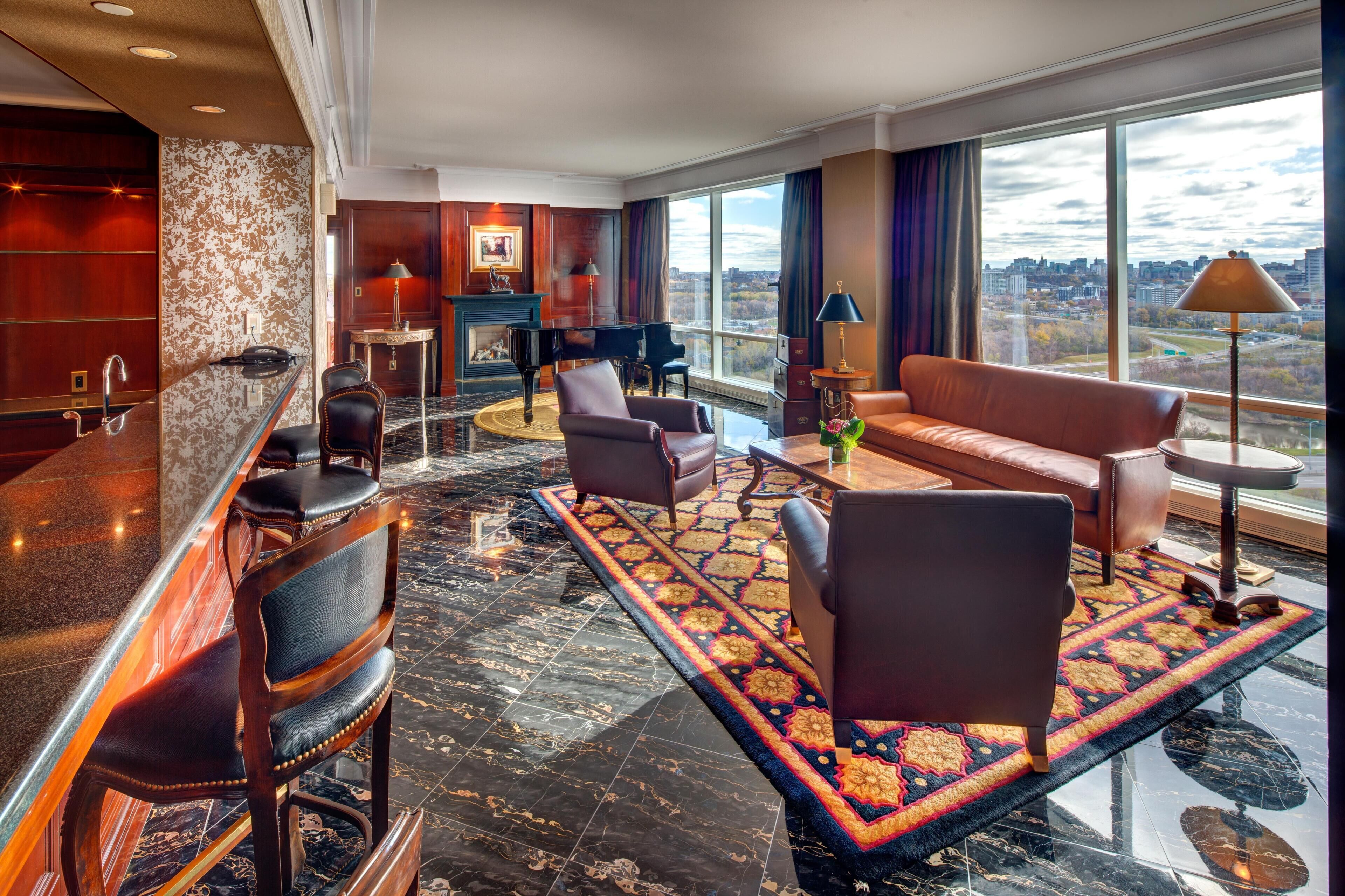 Un vestíbulo de hotel con bar, zona de estar, piano y grandes ventanales que ofrecen vistas a la ciudad.
