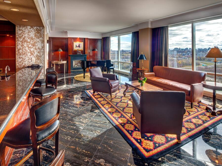 Un vestíbulo de hotel con bar, zona de estar, piano y grandes ventanales que ofrecen vistas a la ciudad.