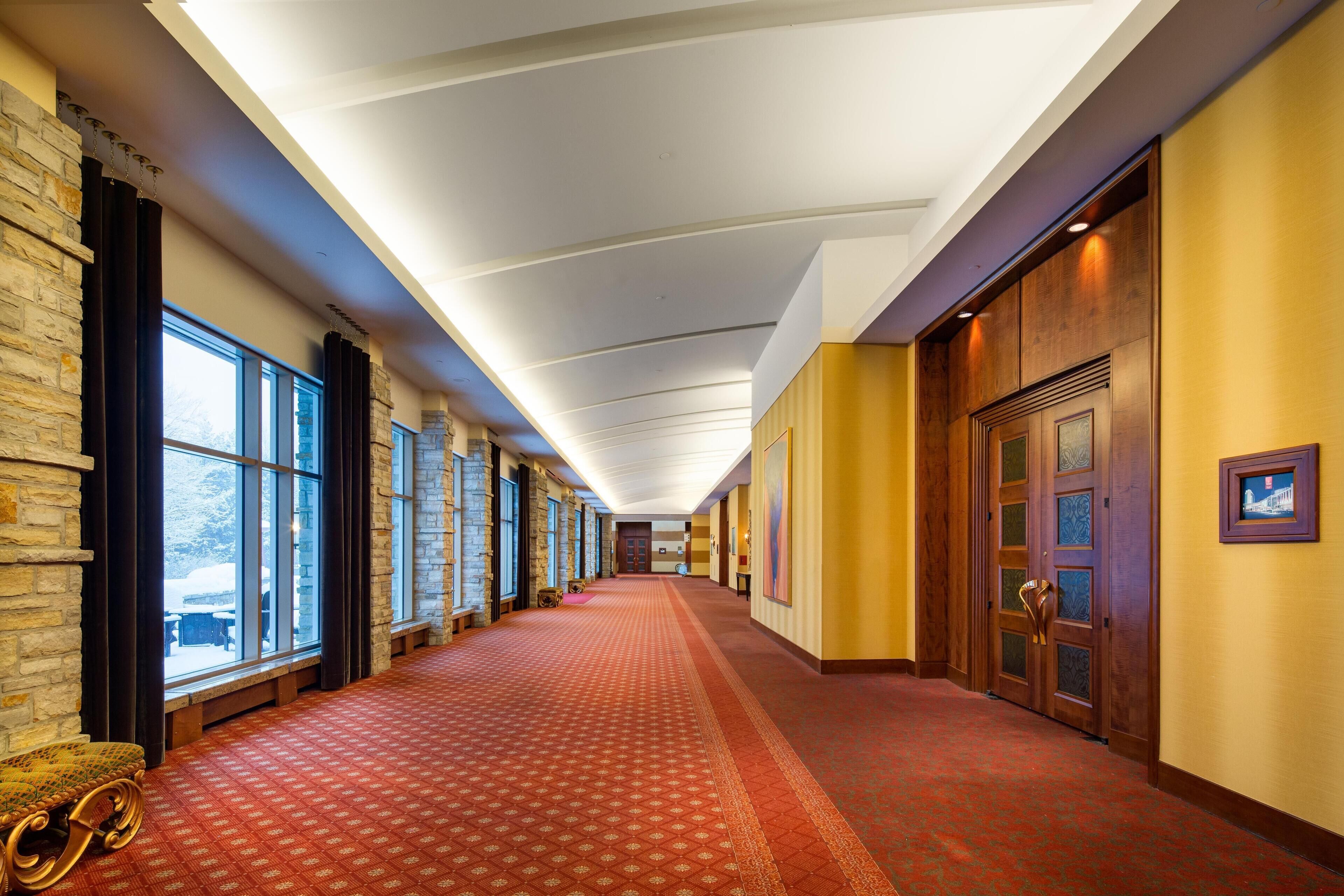 Un pasillo de hotel con paredes de piedra, ventanas amplias y una alfombra roja.