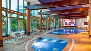 Un área de piscina interior con varias piscinas, zonas de descanso y amplios ventanales.