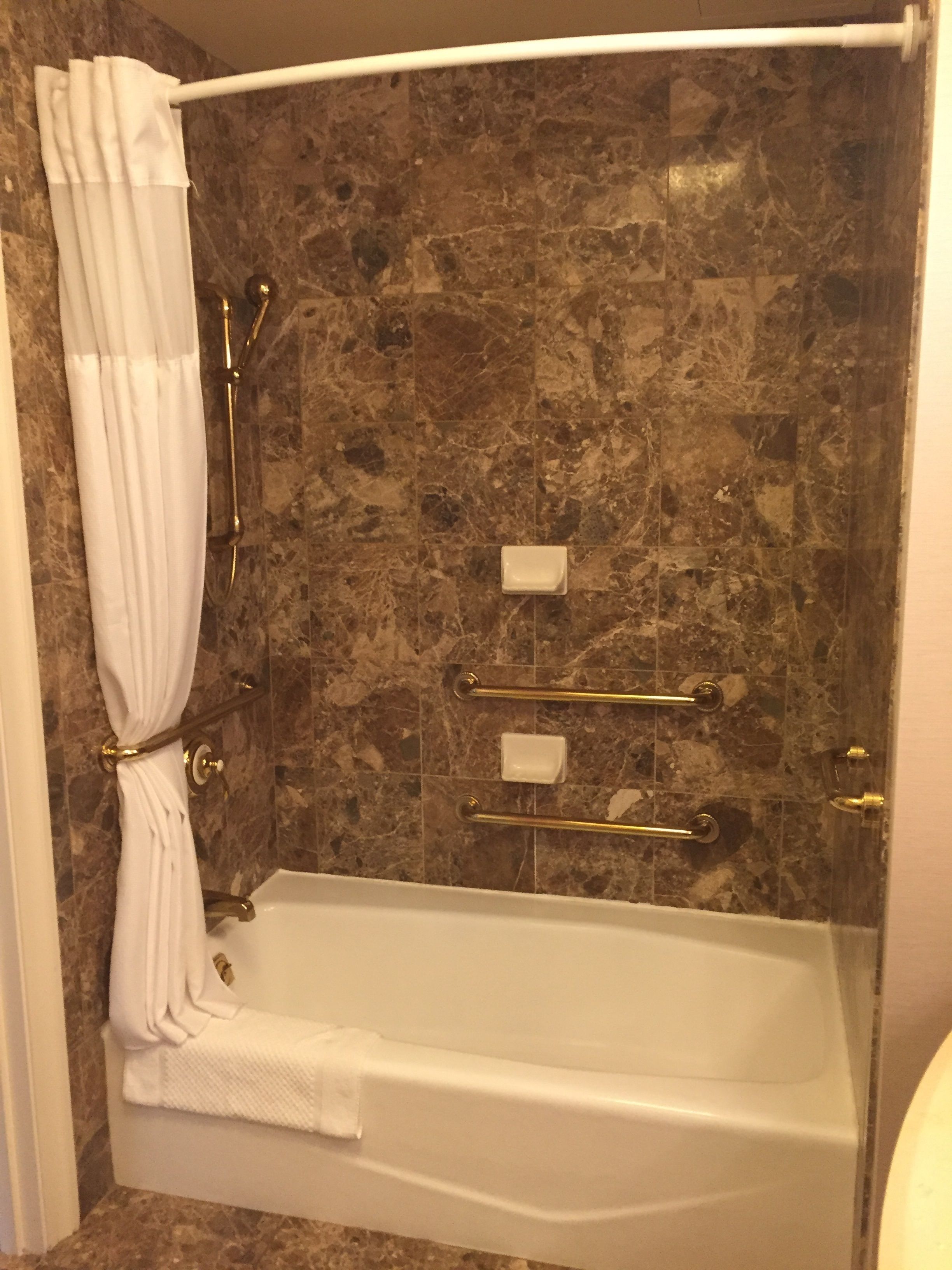 A bathtub with a shower curtain, marble walls, and grab bars.
