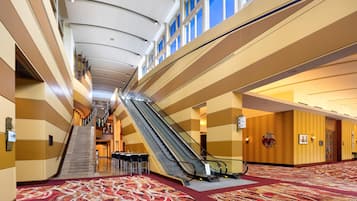 Un vestíbulo de hotel con una escalera mecánica central, una escalera y suelo alfombrado.