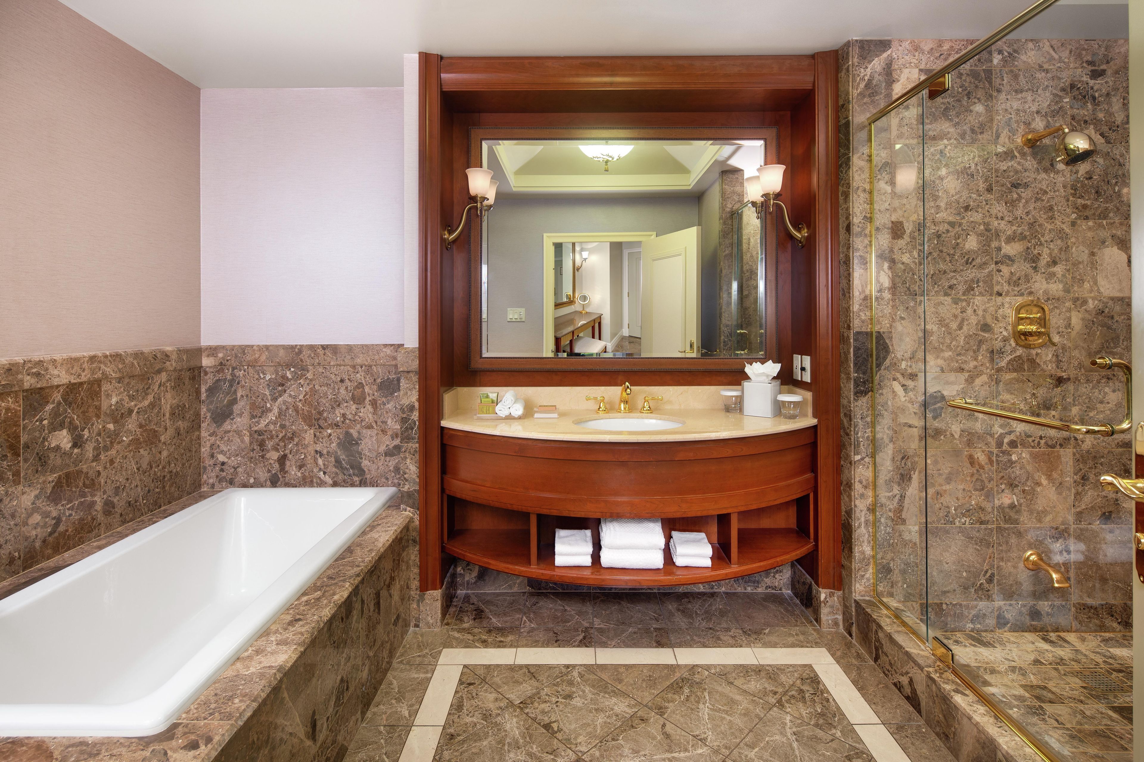 A bathroom with a bathtub, a sink with a vanity, a shower with a glass door, and a mirror above the sink.