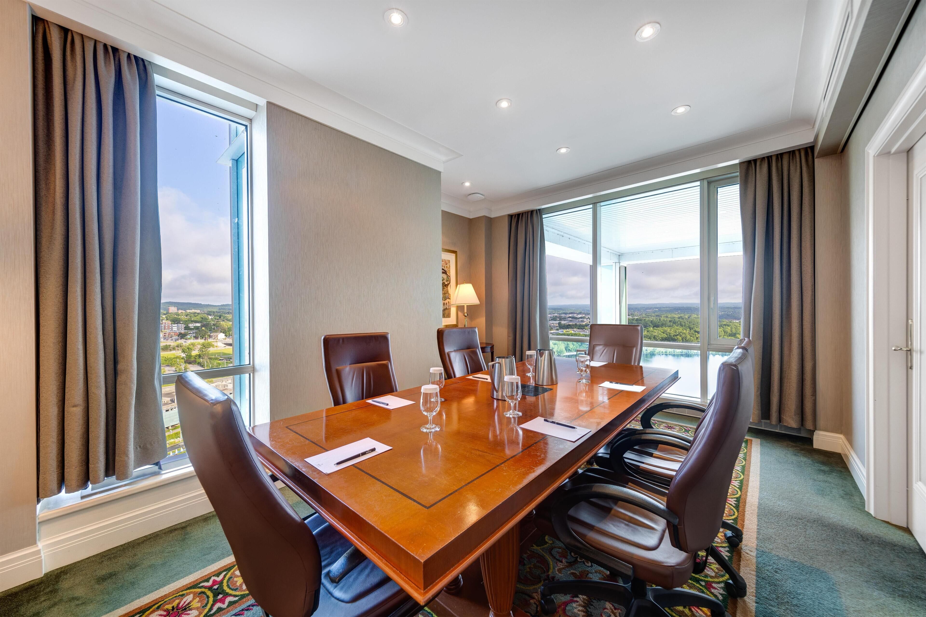 A conference room with a large table, chairs, and large windows with curtains.