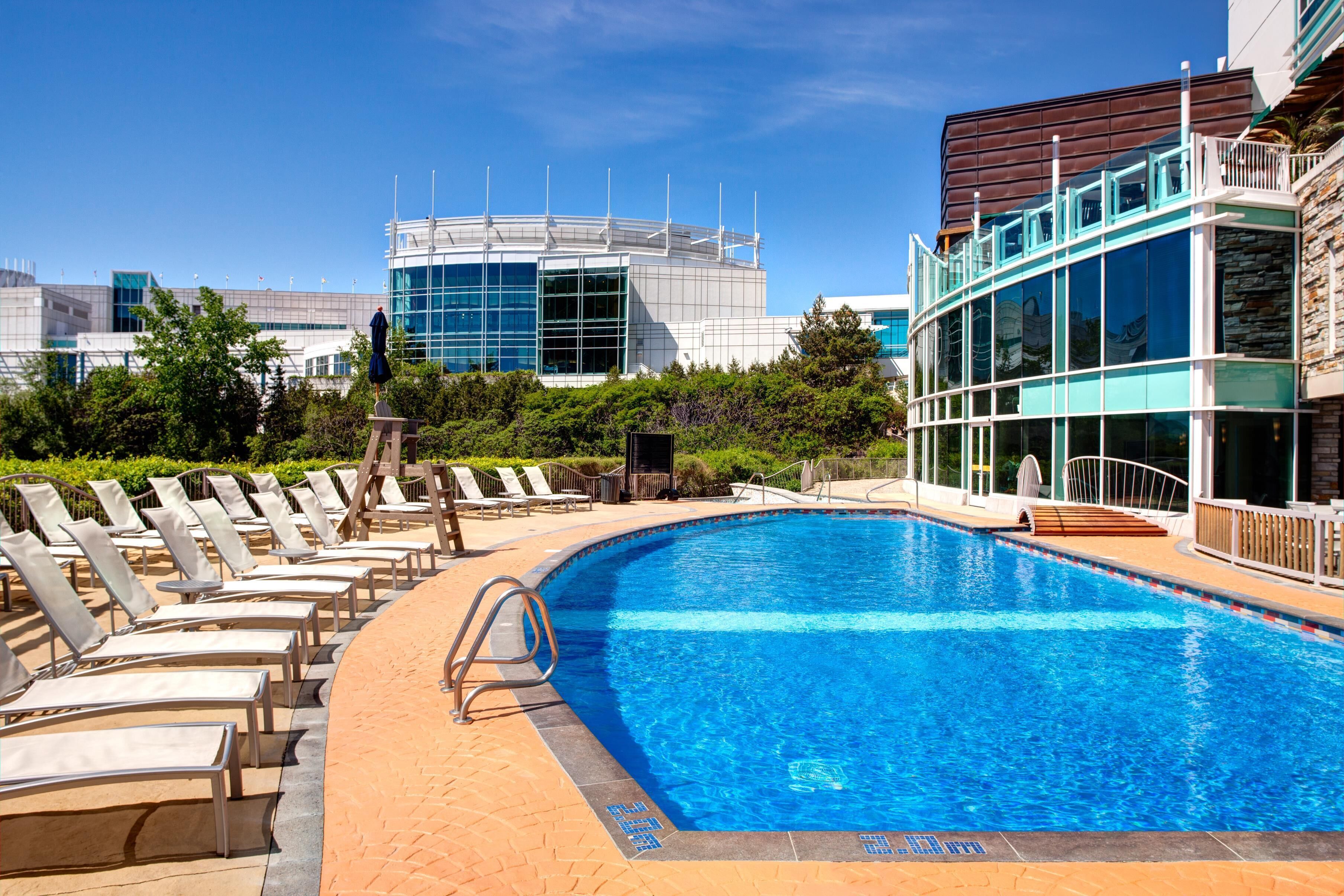 A swimming pool with lounge chairs, a modern building with a glass facade, and a clear blue sky.