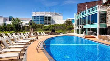 A swimming pool with lounge chairs, a modern building with a glass facade, and a clear blue sky.
