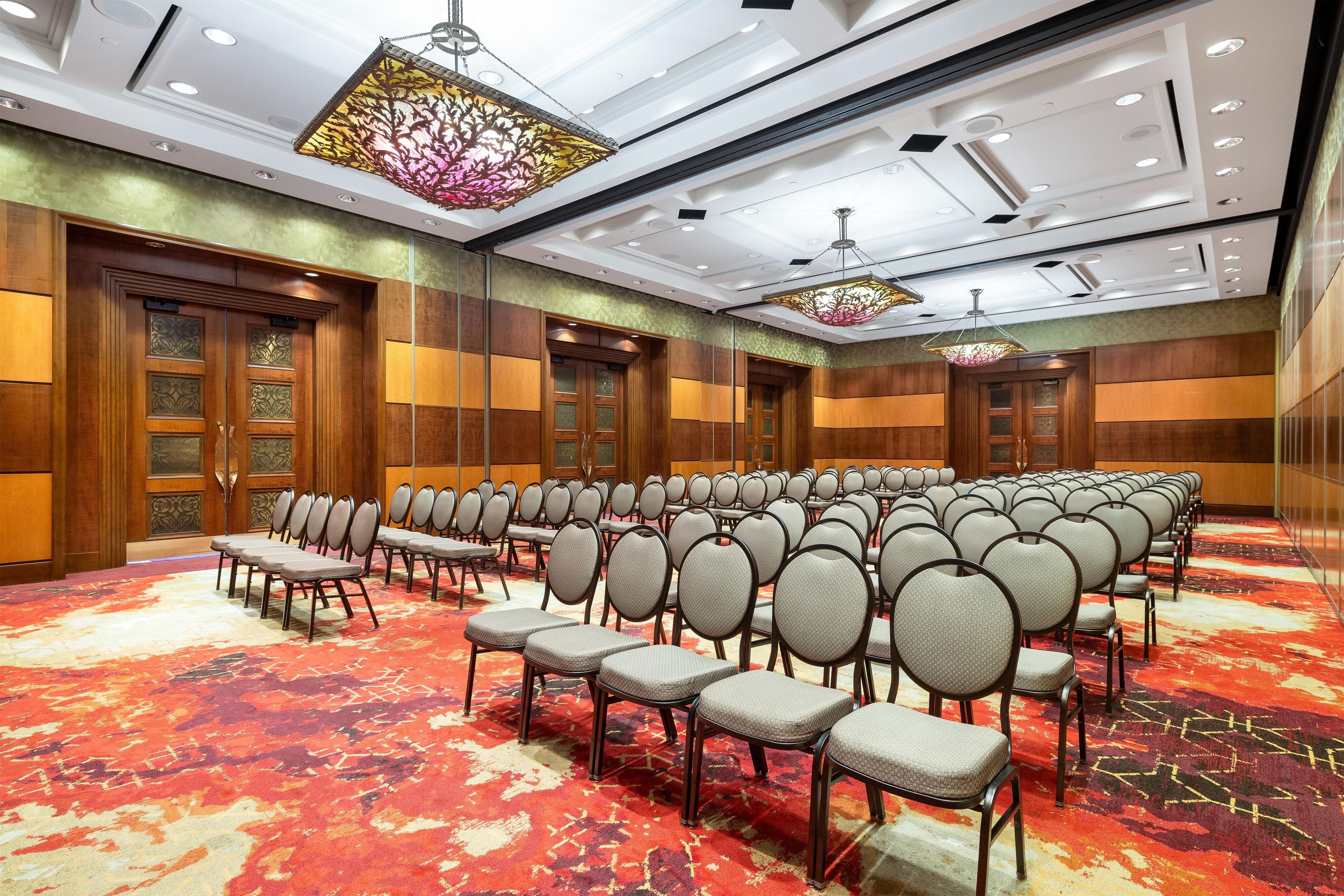 Un salón de conferencias con filas de sillas, paneles de madera y luminarias decorativas.