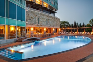 Un hotel con piscina, fachada de piedra y una zona cubierta con sillones de descanso.