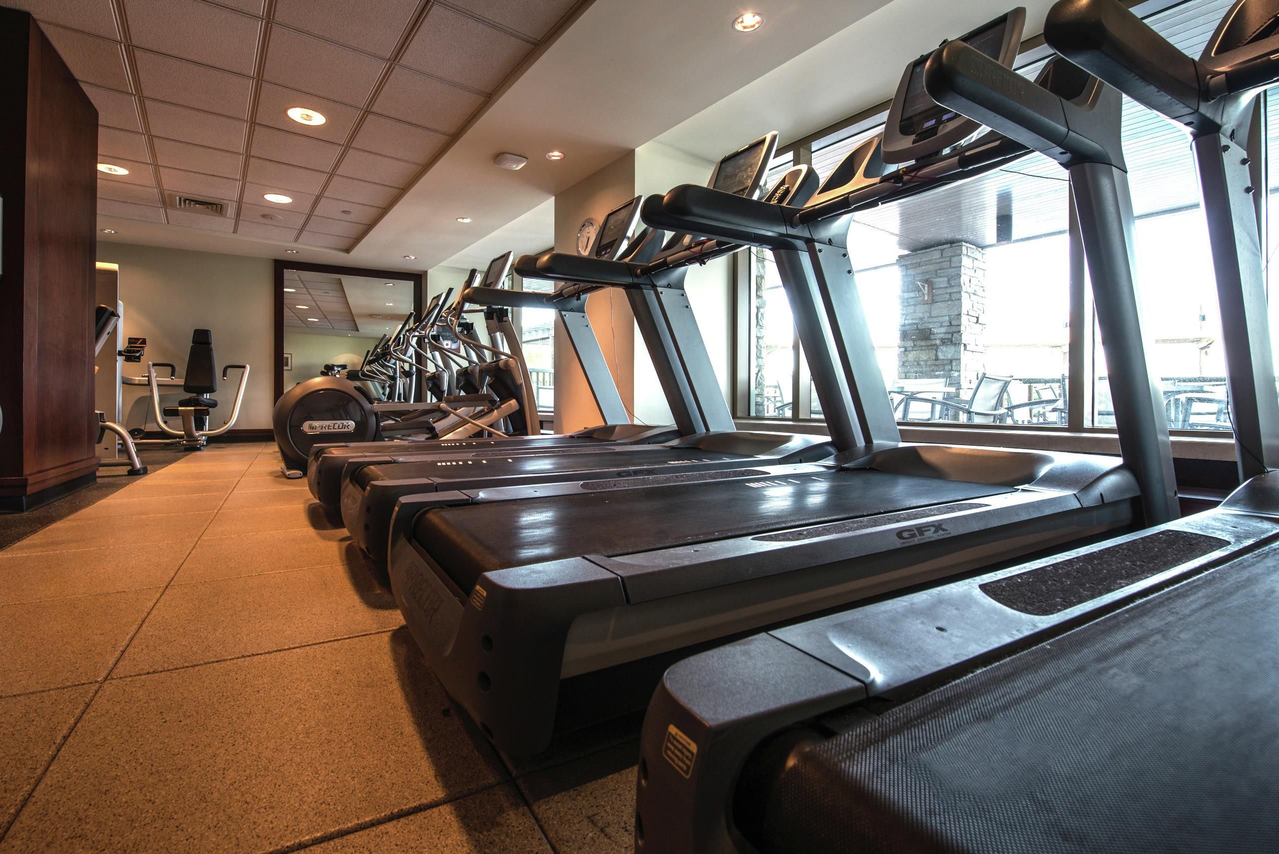 Une salle de sport équipée de plusieurs tapis de course, de vélos d’exercice et d’un mur recouvert de miroirs.