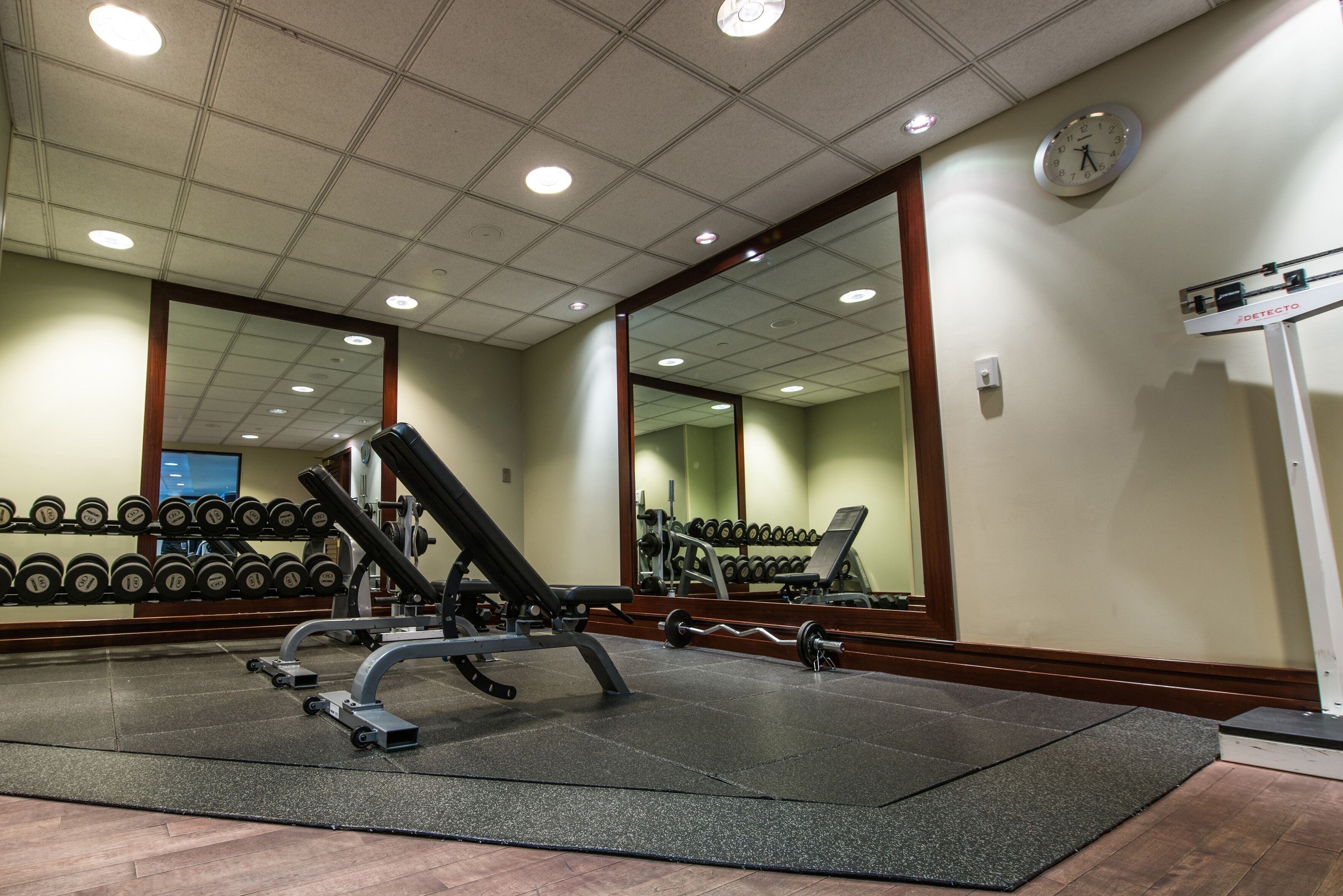 Uma academia com equipamentos de musculação, um espelho e um relógio na parede.