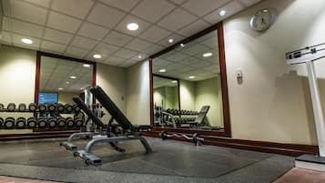 Uma academia com equipamentos de musculação, um espelho e um relógio na parede.