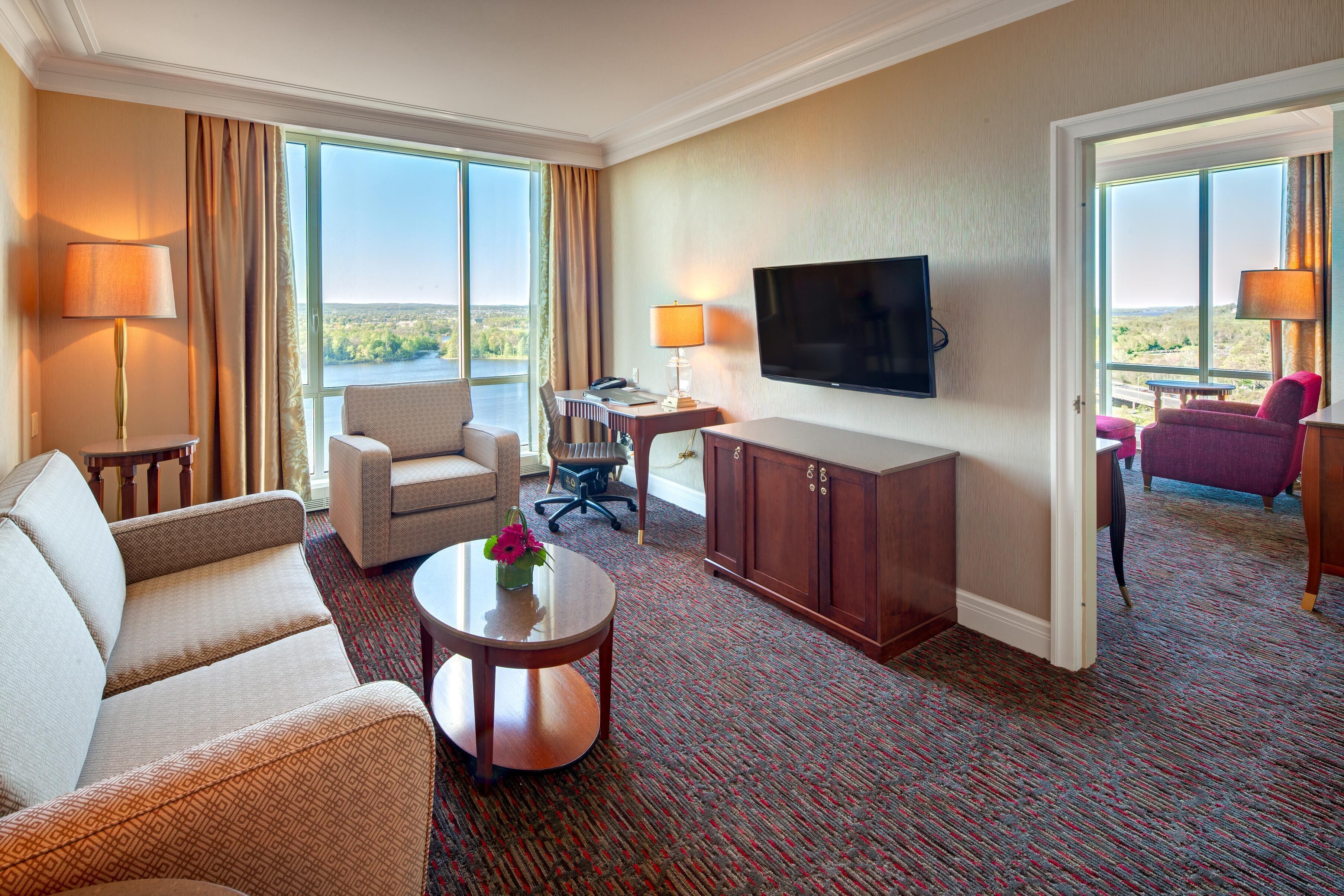 Habitación de hotel con sofá, sillón, mesa de comedor, televisor y vistas al exterior.