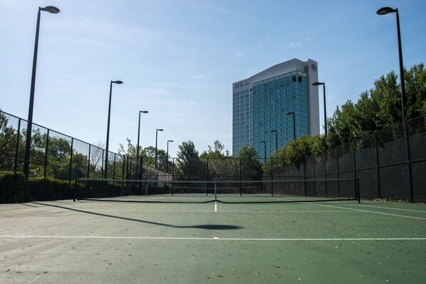 A tennis court with a net, surrounded by a fence and street lamps.