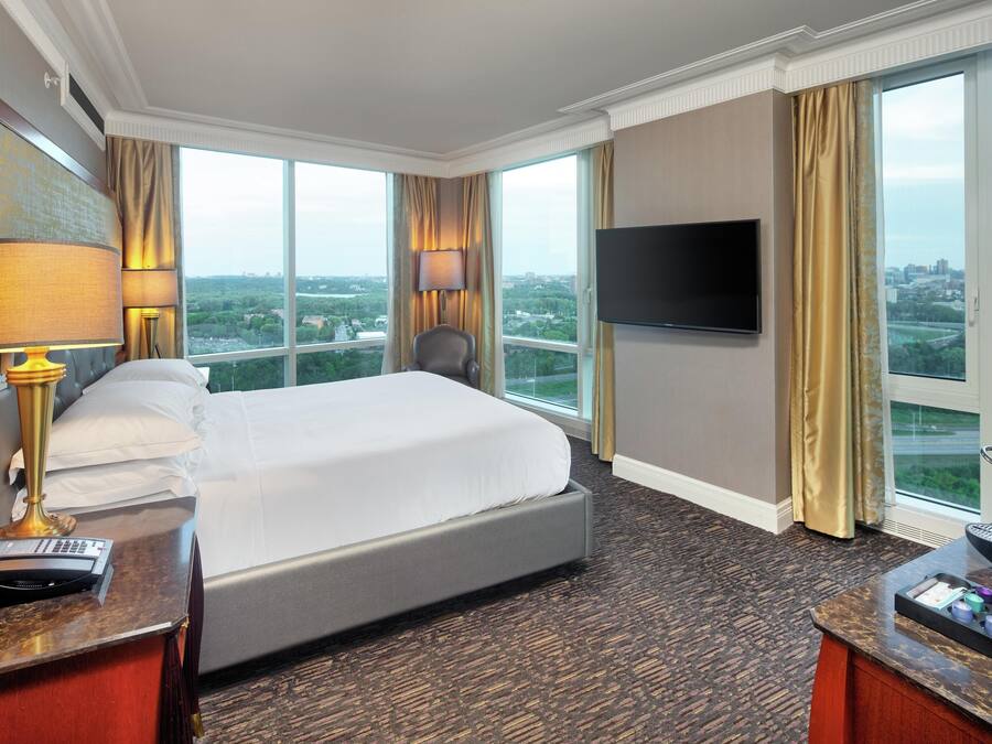 Een hotelkamer met een groot bed, een bureau met lamp, een televisie en uitzicht op de stad.
