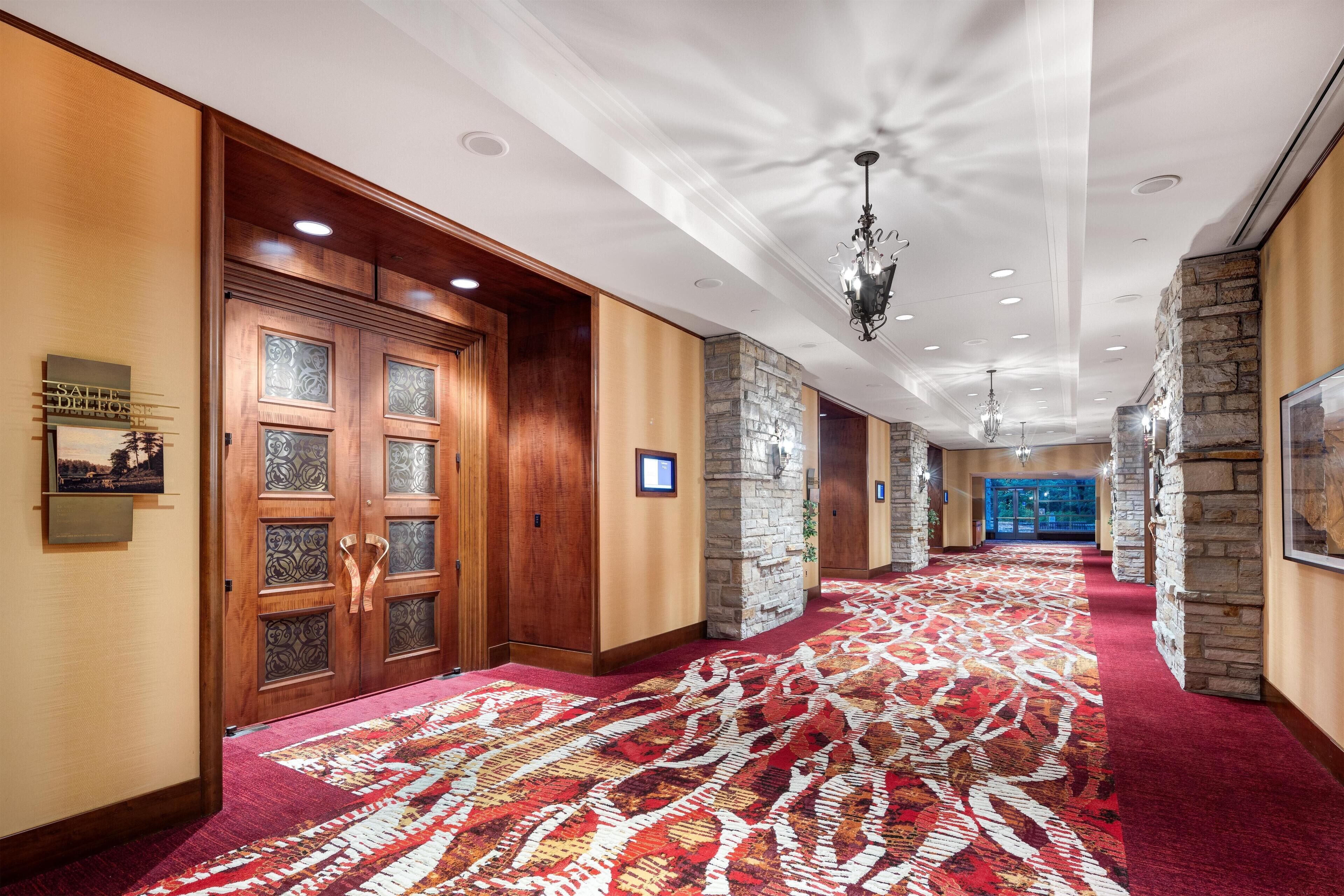Un pasillo de hotel con alfombra estampada, puertas de madera, detalles de piedra y un candelabro.