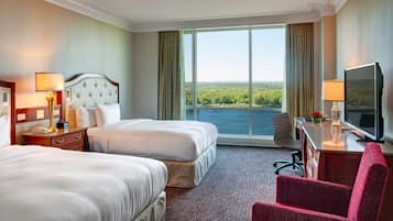 Habitación de hotel con dos camas, un escritorio con televisor y vista a un lago.