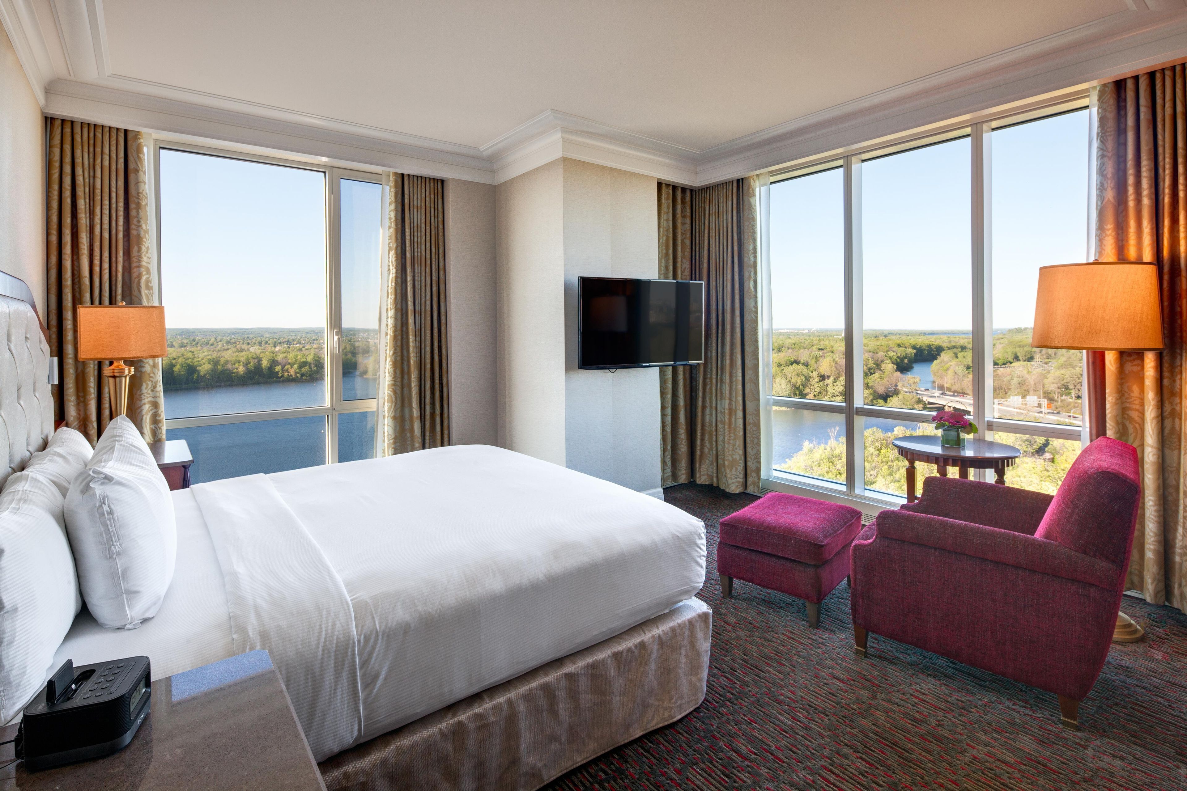 Una habitación de hotel con una cama grande, un televisor de pantalla plana, un escritorio con teléfono, una silla y vista a un lago.