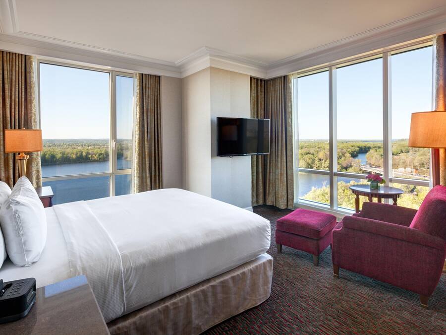 Una habitación de hotel con una cama grande, un televisor de pantalla plana, un escritorio con teléfono, una silla y vista a un lago.