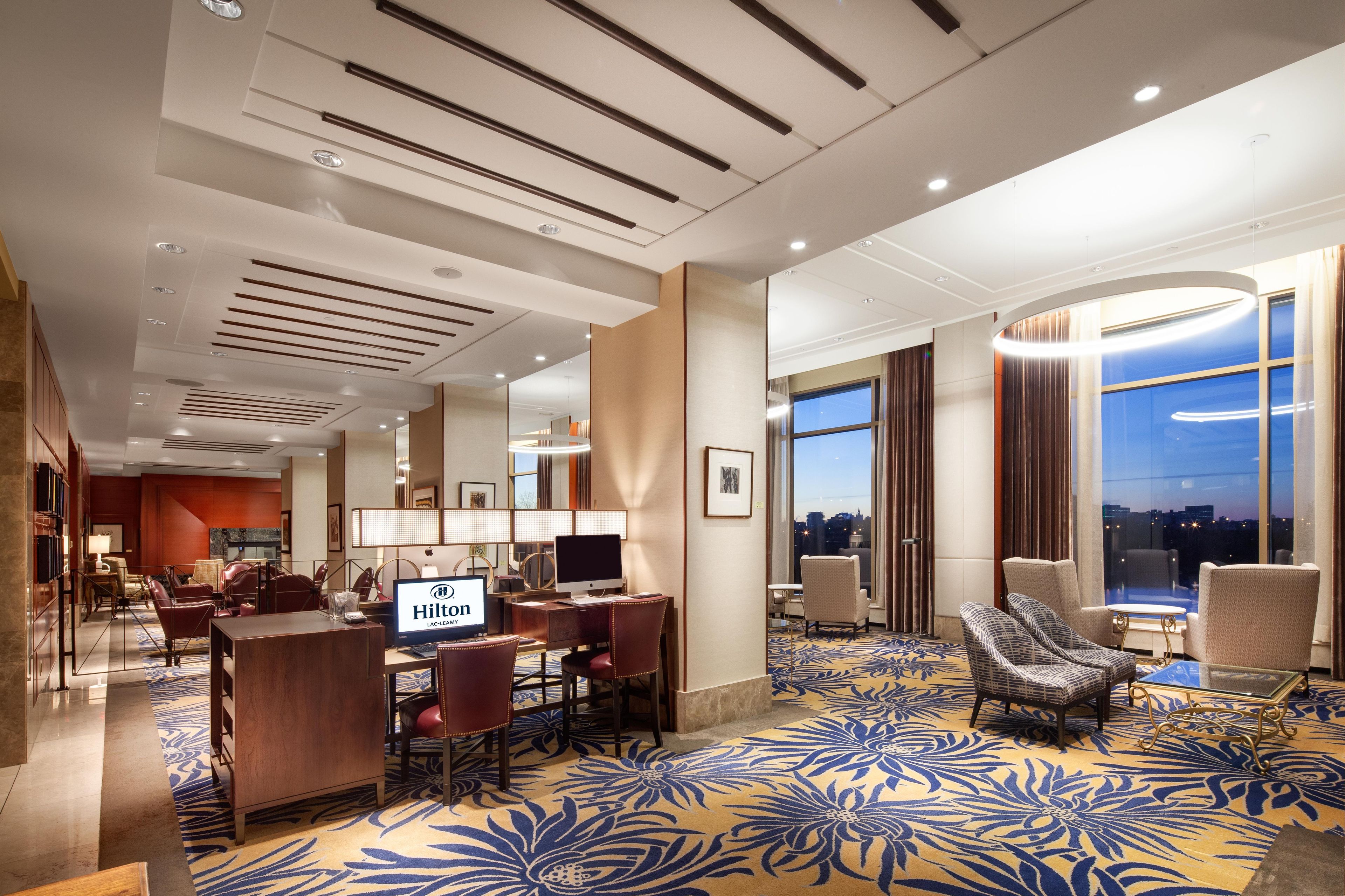 A hotel room with a desk, computer, and seating area.