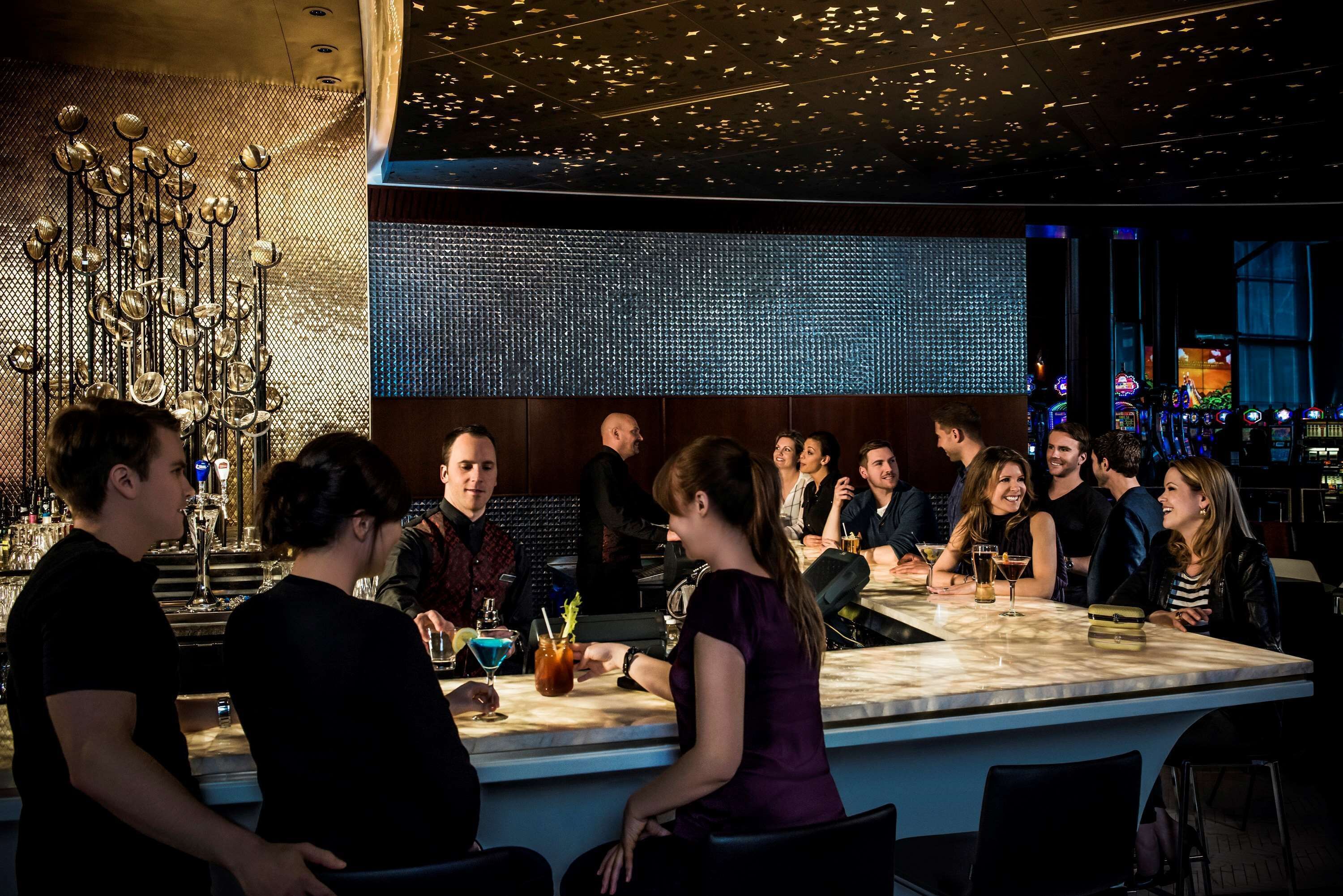 Un espace bar doté d’un comptoir en marbre, de luminaires suspendus et d’un écran numérique en arrière-plan.