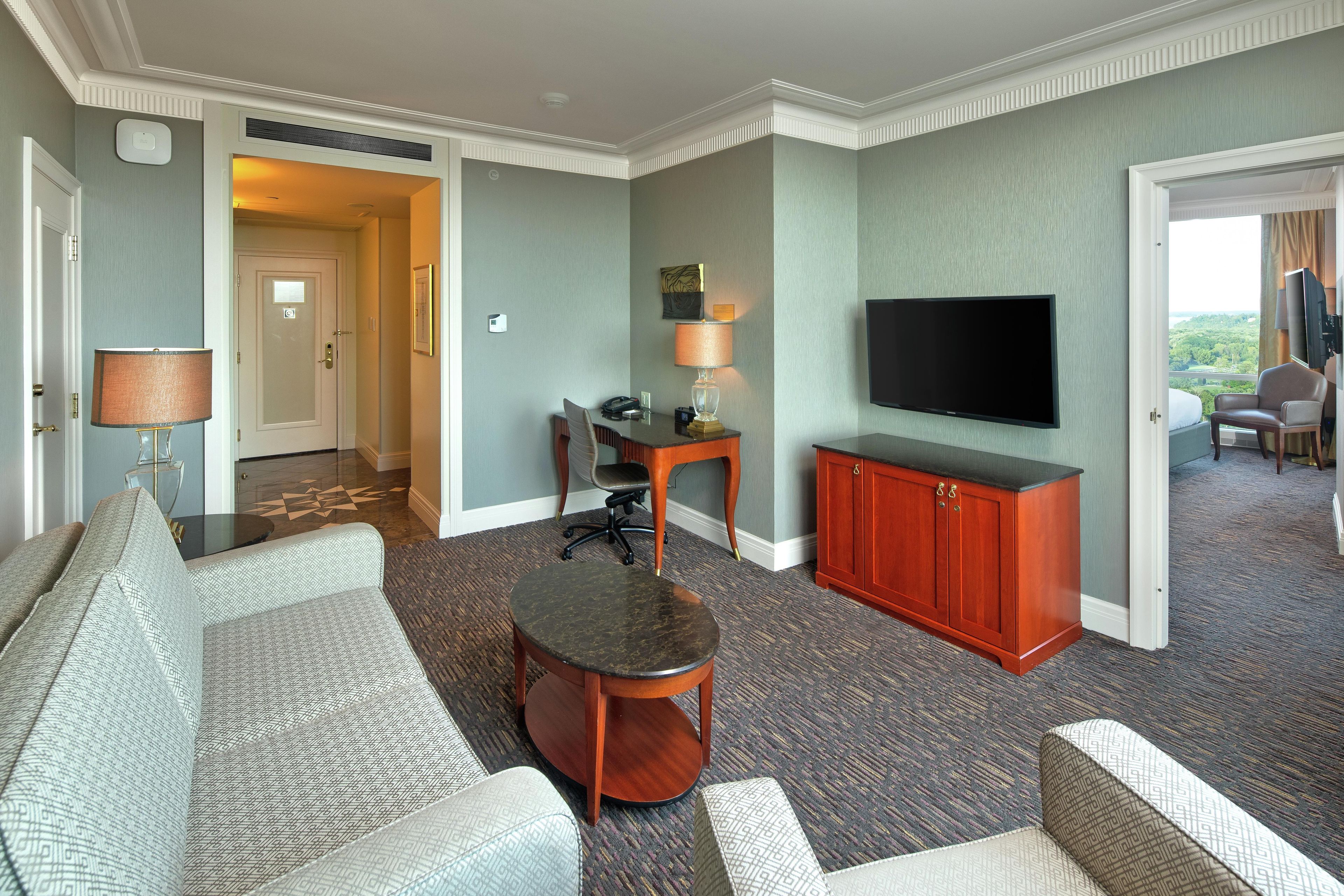 A hotel room with a sofa, a round coffee table, a TV, a desk with a lamp, and a cabinet.