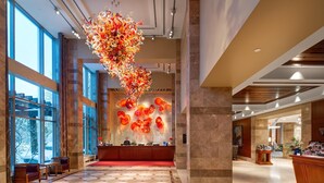 Et hotellobby med reception, siddeområde, store vinduer og en dekorativ vægkunst.