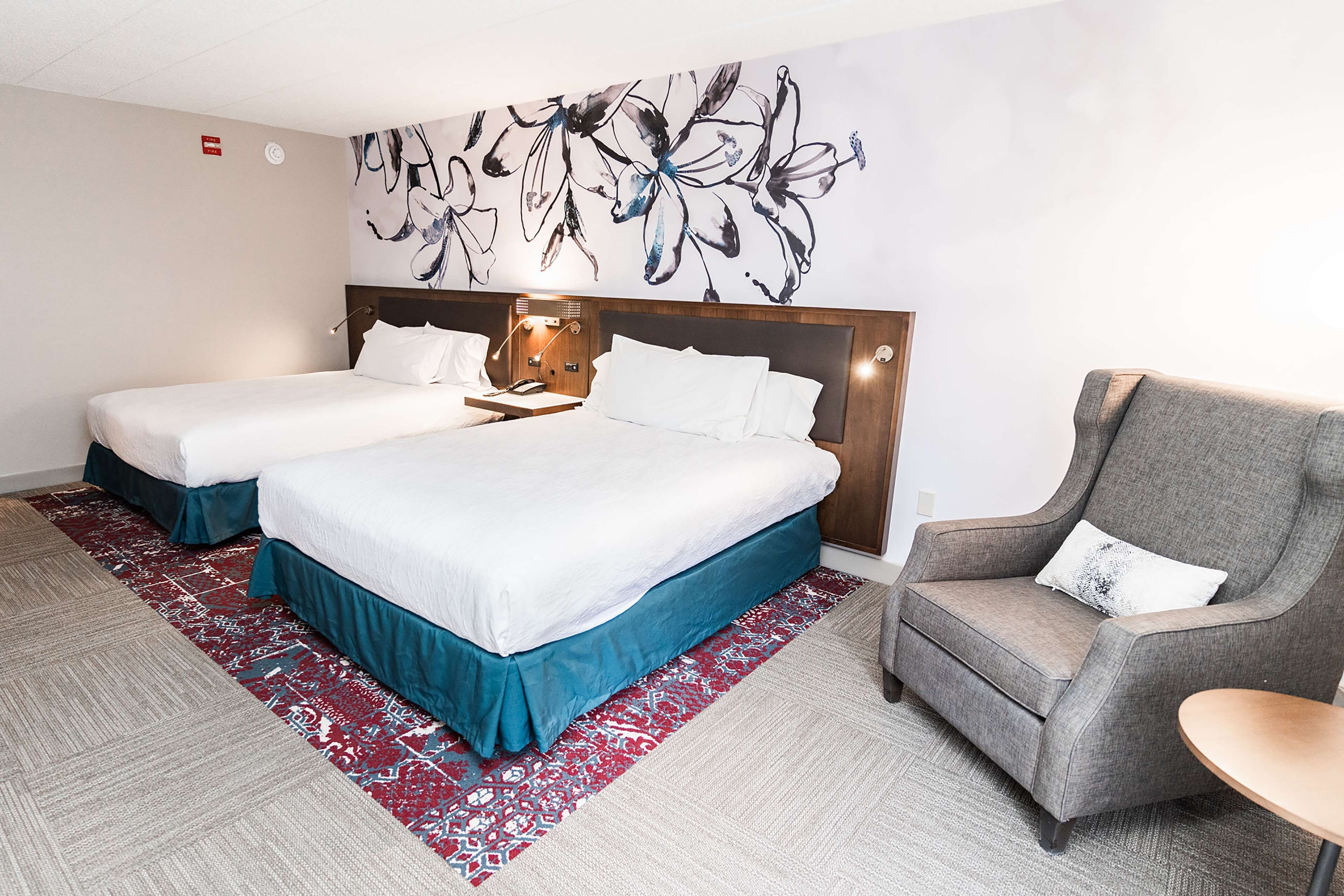Habitación de hotel con dos camas, un sofá, una mesita y una pared con un mural floral.
