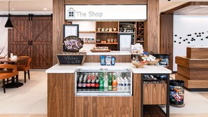 A shop counter with a refrigerated display of beverages, shelves stocked with snacks, and a chalkboard menu. - Hilton Garden Inn Fairfax (Fairfax)