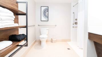 Ein modernes Badezimmer mit Toilette, Ablagefläche mit Handtüchern, Mülleimer und Duschbereich.