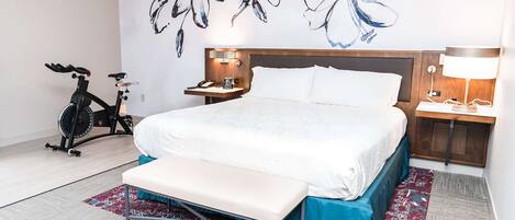 Una habitación de hotel con una cama, un banco, una bicicleta y un cuadro floral en la pared.
