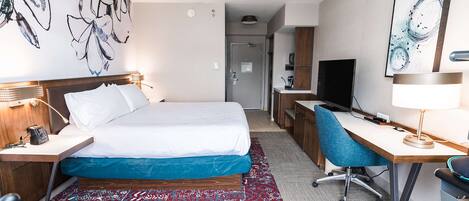 A hotel room with a bed, desk, chair, and a TV.