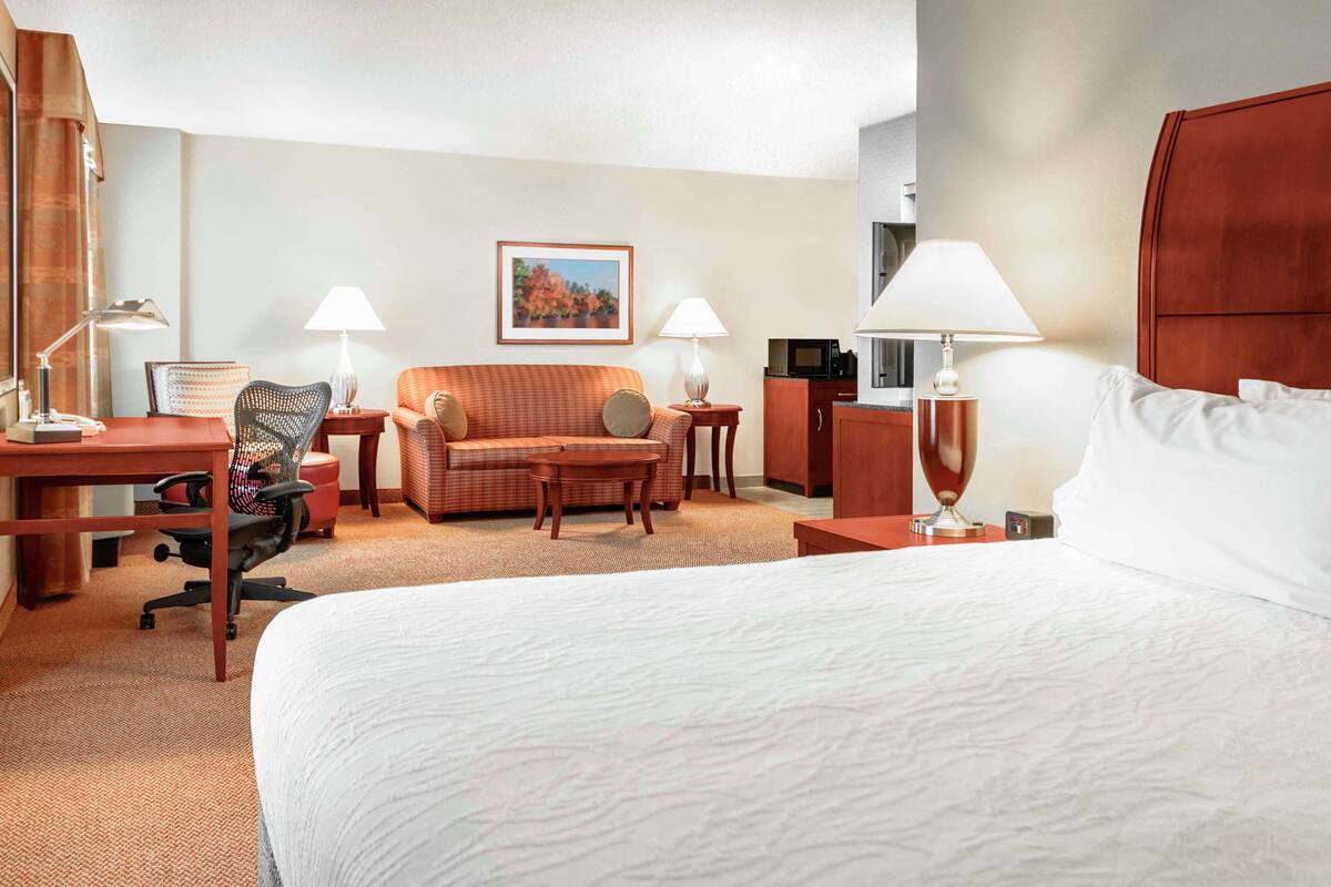 A hotel room with a large bed, a desk, a chair, a sofa, and two lamps.