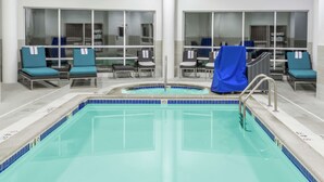 Ein Poolbereich mit Liegestühlen, einem überdachten Stuhl, Glaswänden und einer gefliesten Poolkante.