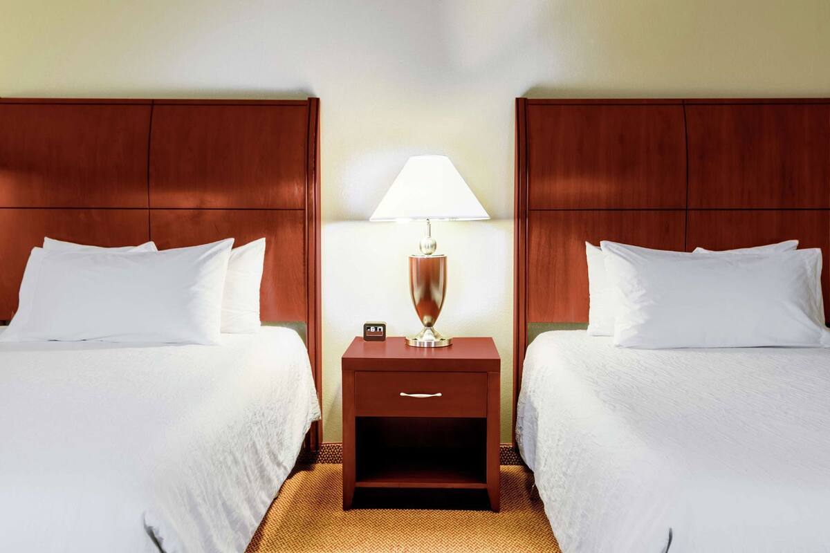 A hotel room with two beds, a nightstand with a lamp, and a digital clock.