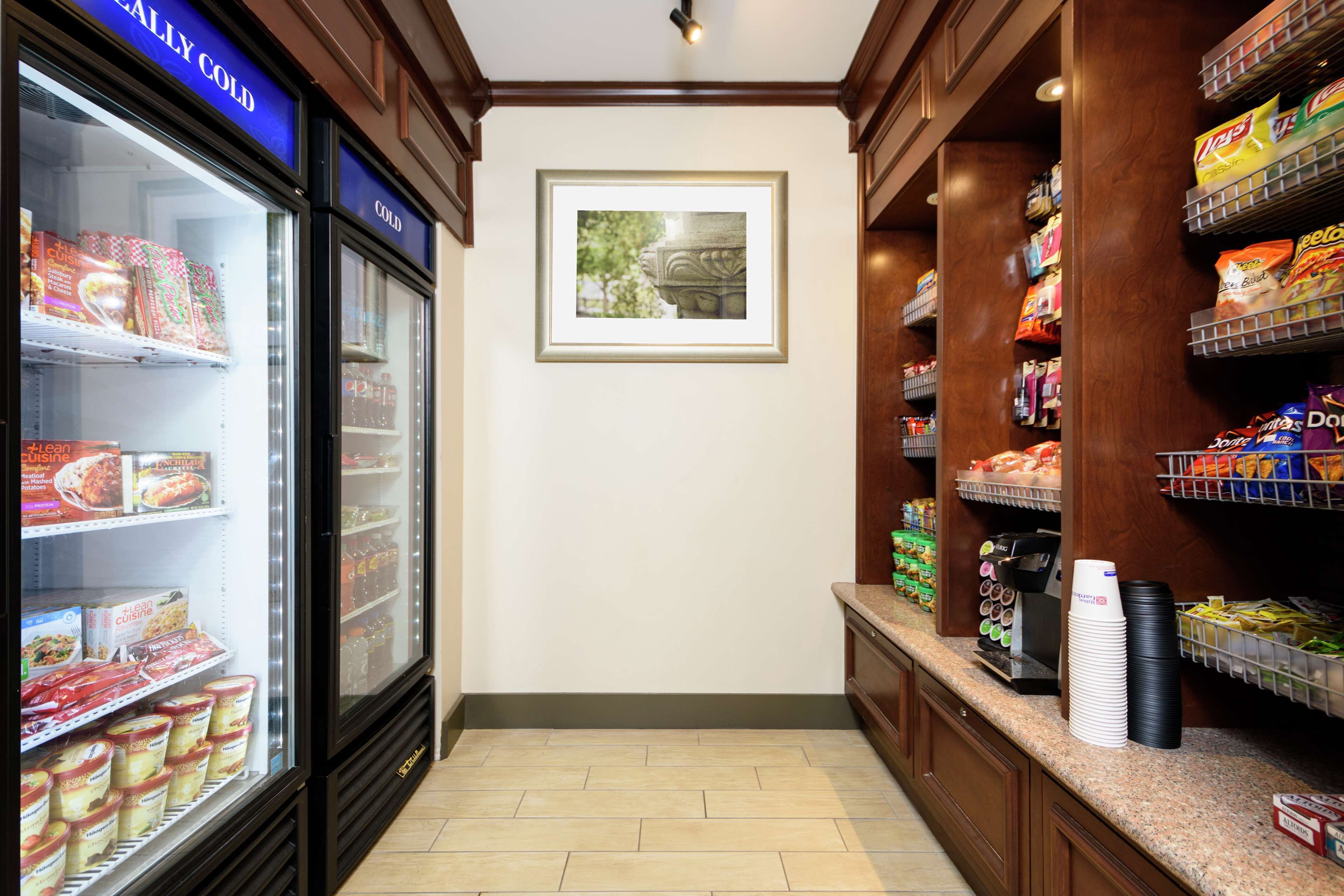 Ein Hotel-Lagerraum mit Regalen voller Snacks und Getränke, einer Kaffeemaschine und einem gerahmten Bild an der Wand.