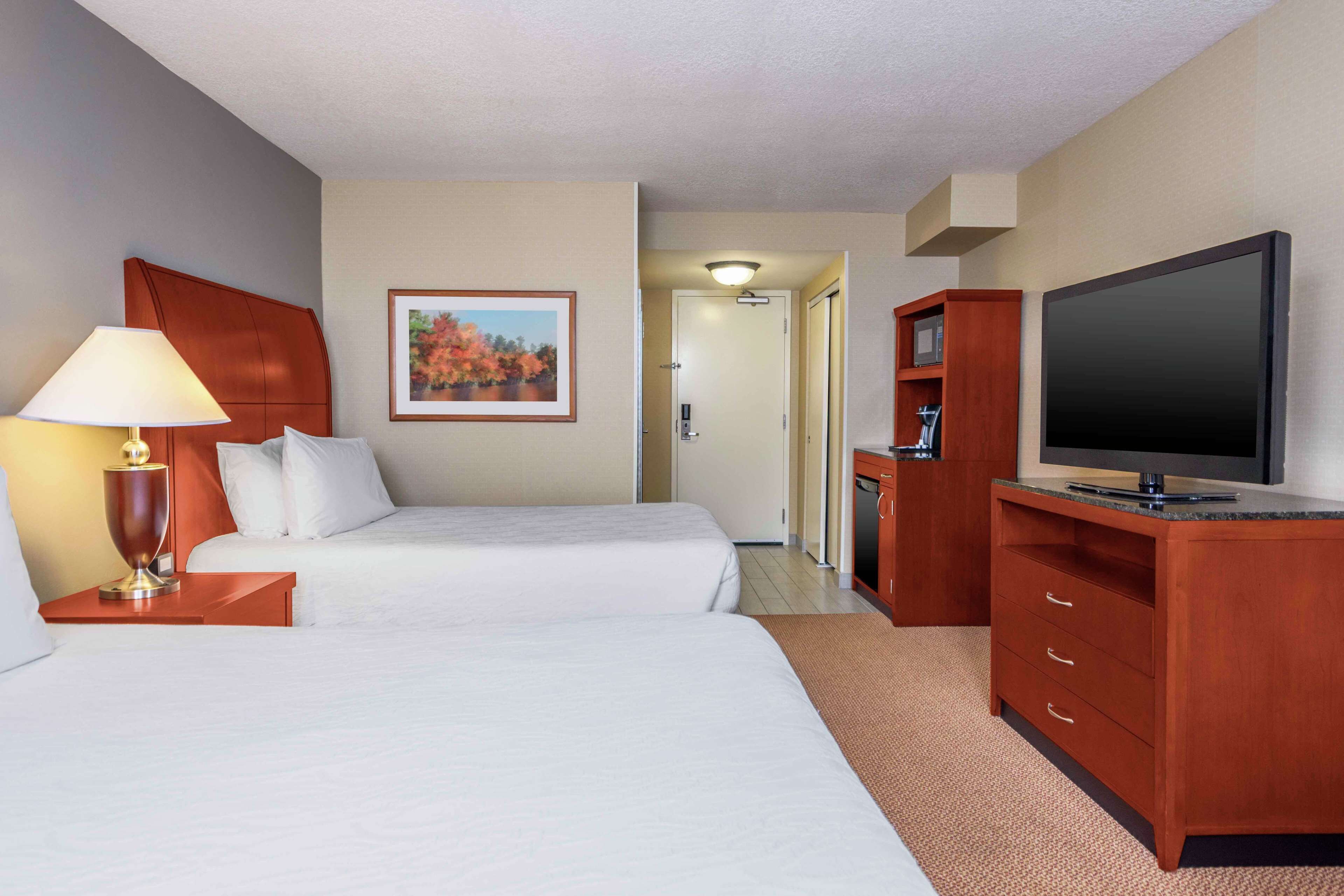 A hotel room with two beds, a TV, a desk with a lamp, and a painting on the wall.
