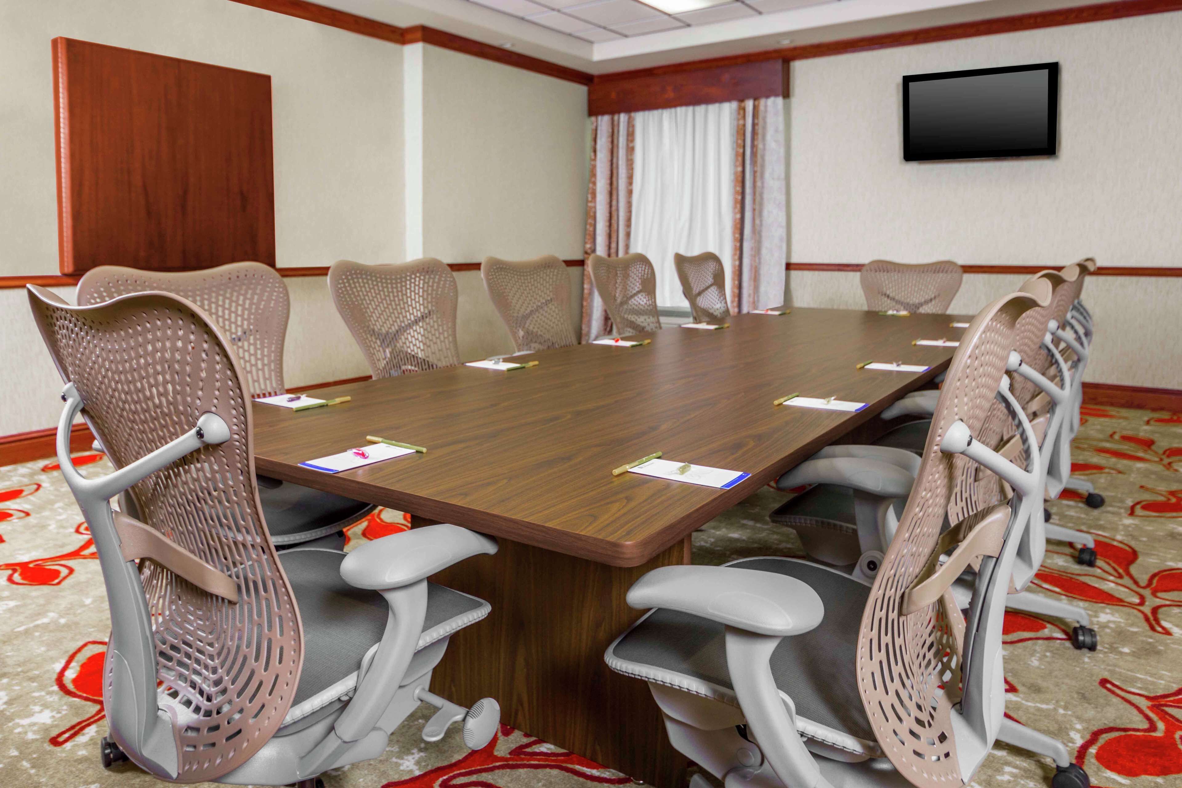 A conference room with a long table, six chairs, and a flat-screen TV on the wall.