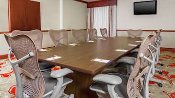 A conference room with a long table, six chairs, and a flat-screen TV on the wall.