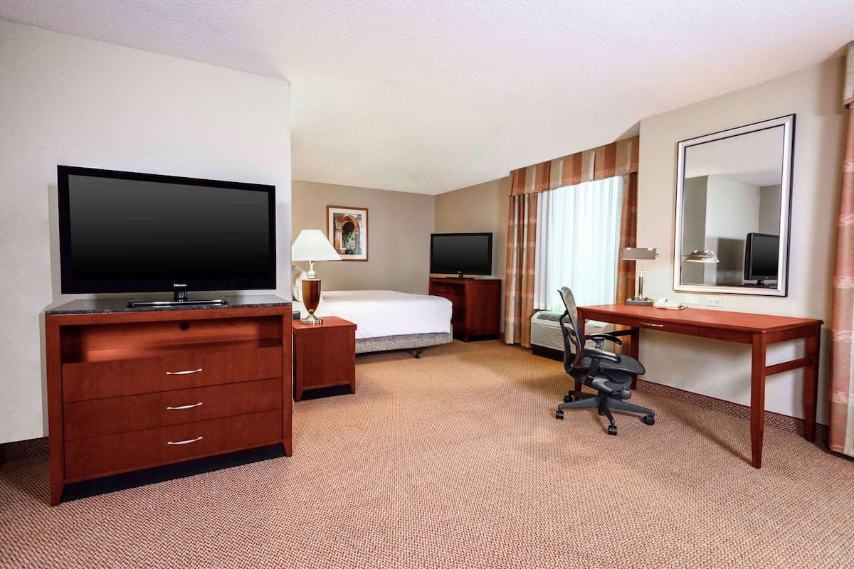 Ein Hotelzimmer mit Bett, Schreibtisch, Stuhl, Fernseher und Spiegel.