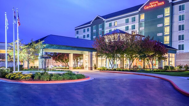 Ein Hilton Garden Inn mit modernem Design, mit großzügigem Eingangsbereich, überdachtem Wartebereich und einem begrünten Zugangsbereich.