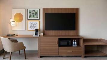 A modern hotel room with a wooden desk, a chair, a flat-screen TV, and a coffee maker.