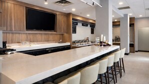 A modern kitchen with a long island counter, bar stools, a flat-screen TV, and a menu board. - Holiday Inn & Suites Mississauga West - Meadowvale (Mississauga)