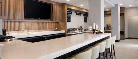 A modern kitchen with a long island counter, bar stools, a flat-screen TV, and a menu board.