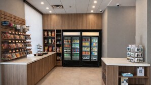 A clean, modern snack bar with a wooden counter, refrigerated drinks, and a variety of packaged snacks. - Holiday Inn & Suites Mississauga West - Meadowvale (Mississauga)